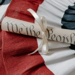 Close-up of a 'We the People' scroll on an American flag cloth background.